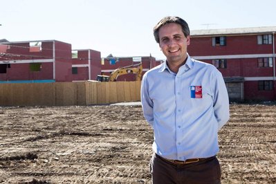 A man with his hands in the back stands in front of newly constructed social houses. 