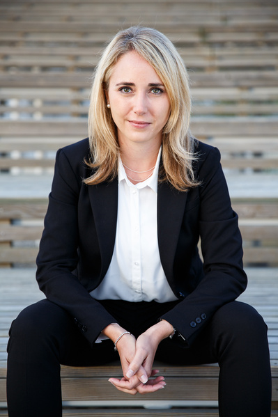 A woman siting on the stairs of an amphitheater with her hands intertwined looks strait to the front