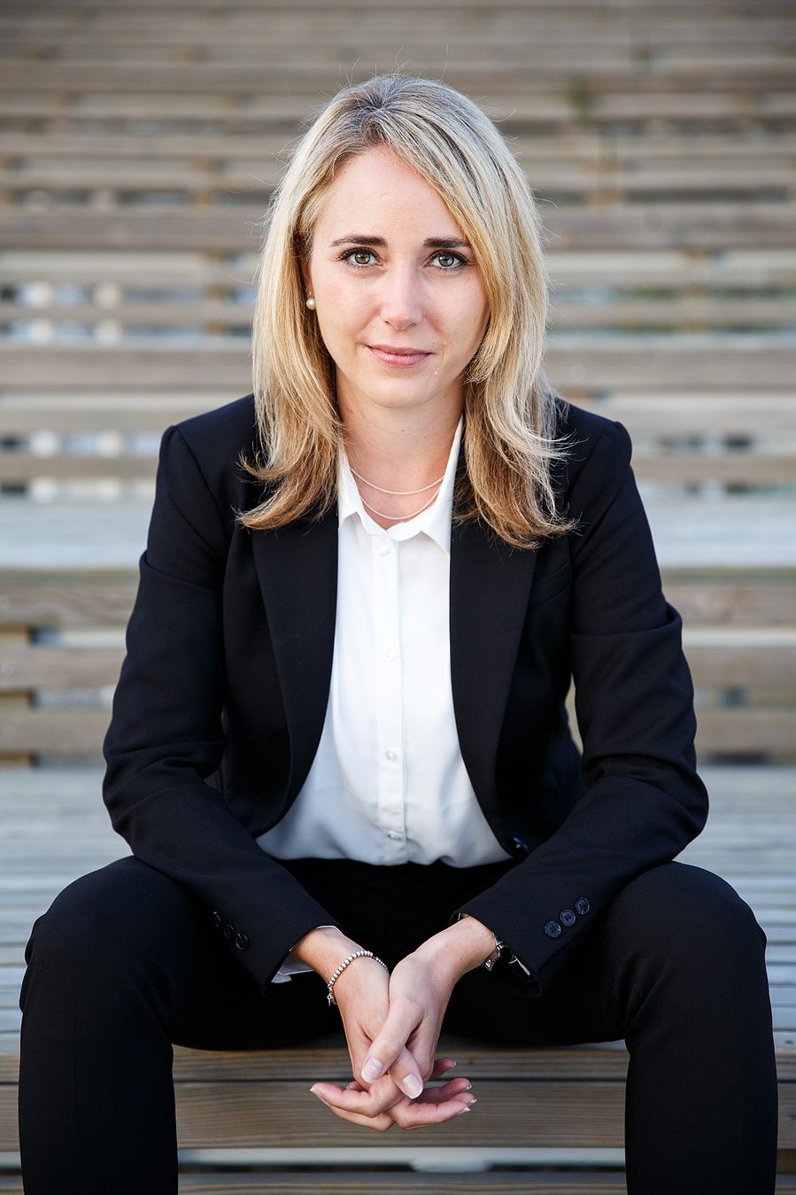 A woman siting on the stairs of an amphitheater with her hands intertwined looks strait to the front