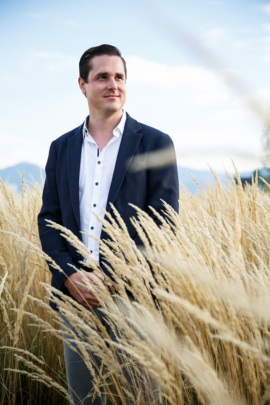 A man in a suit looks to his left side between high yellow grass