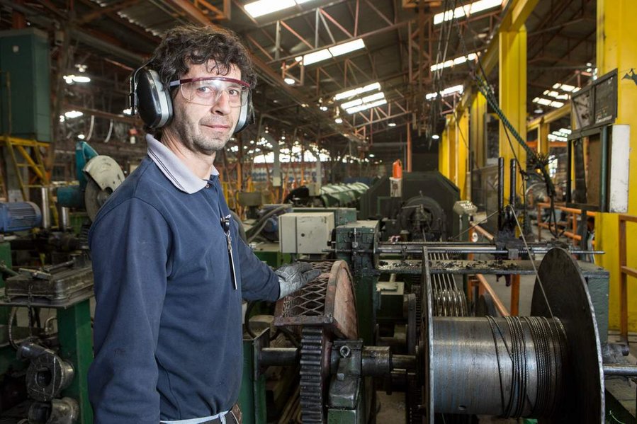 A factory worker stands in front of heavy machinery