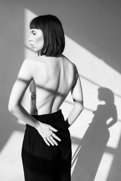 A  woman looks to the side while showing her back and you can see the projection of her sharow too.  