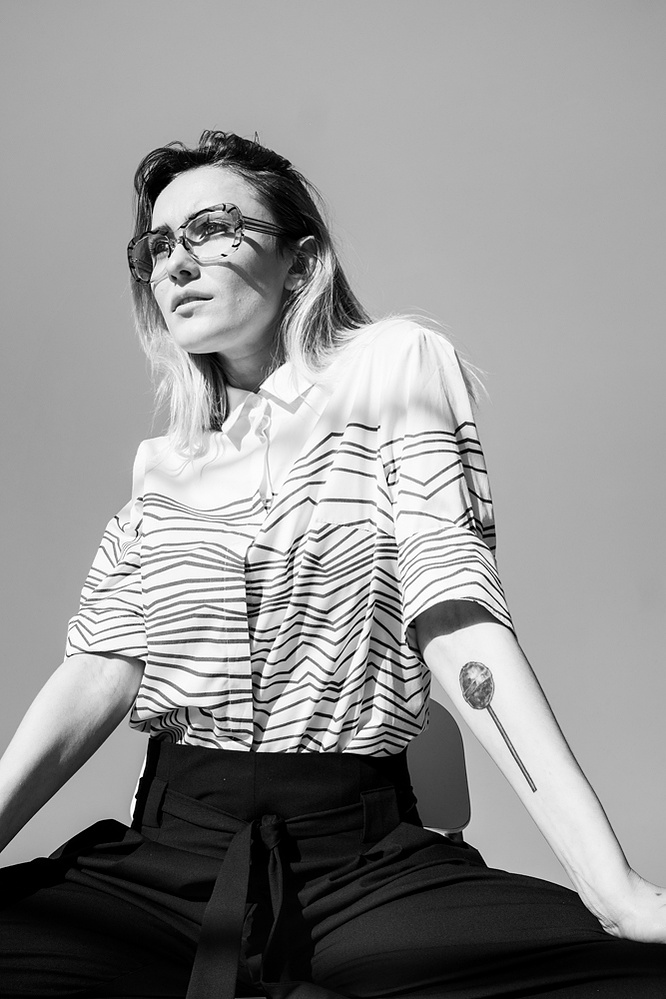 A woman with a lollypop tattoo in her left forearm sits with her arms on her knees 