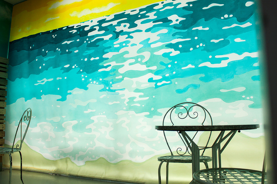A decorative table and chair are silhouetted in front of a glowing beach mural.