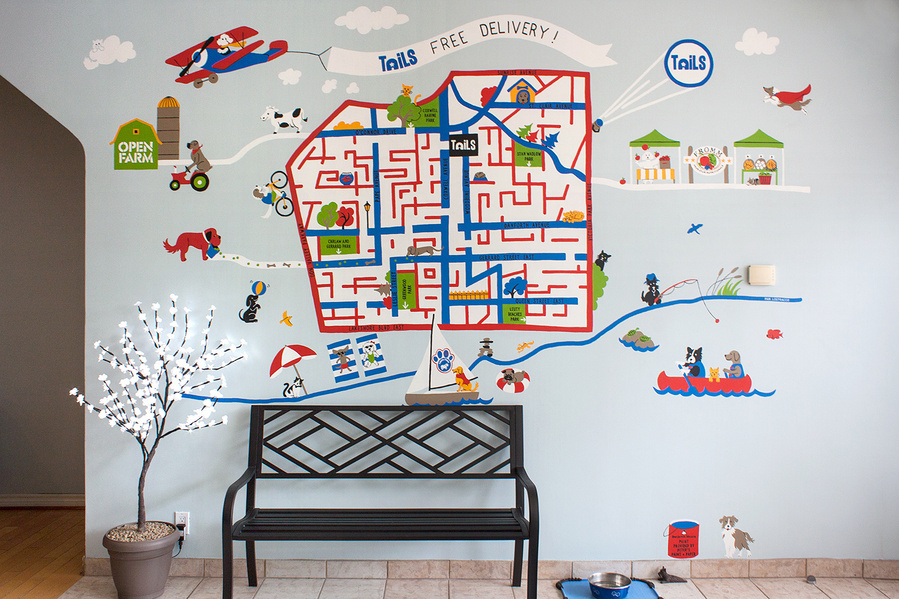 A black bench sits in front of a wall painted with a map turned into a maze. Fun cat and dog characters play in the mural.