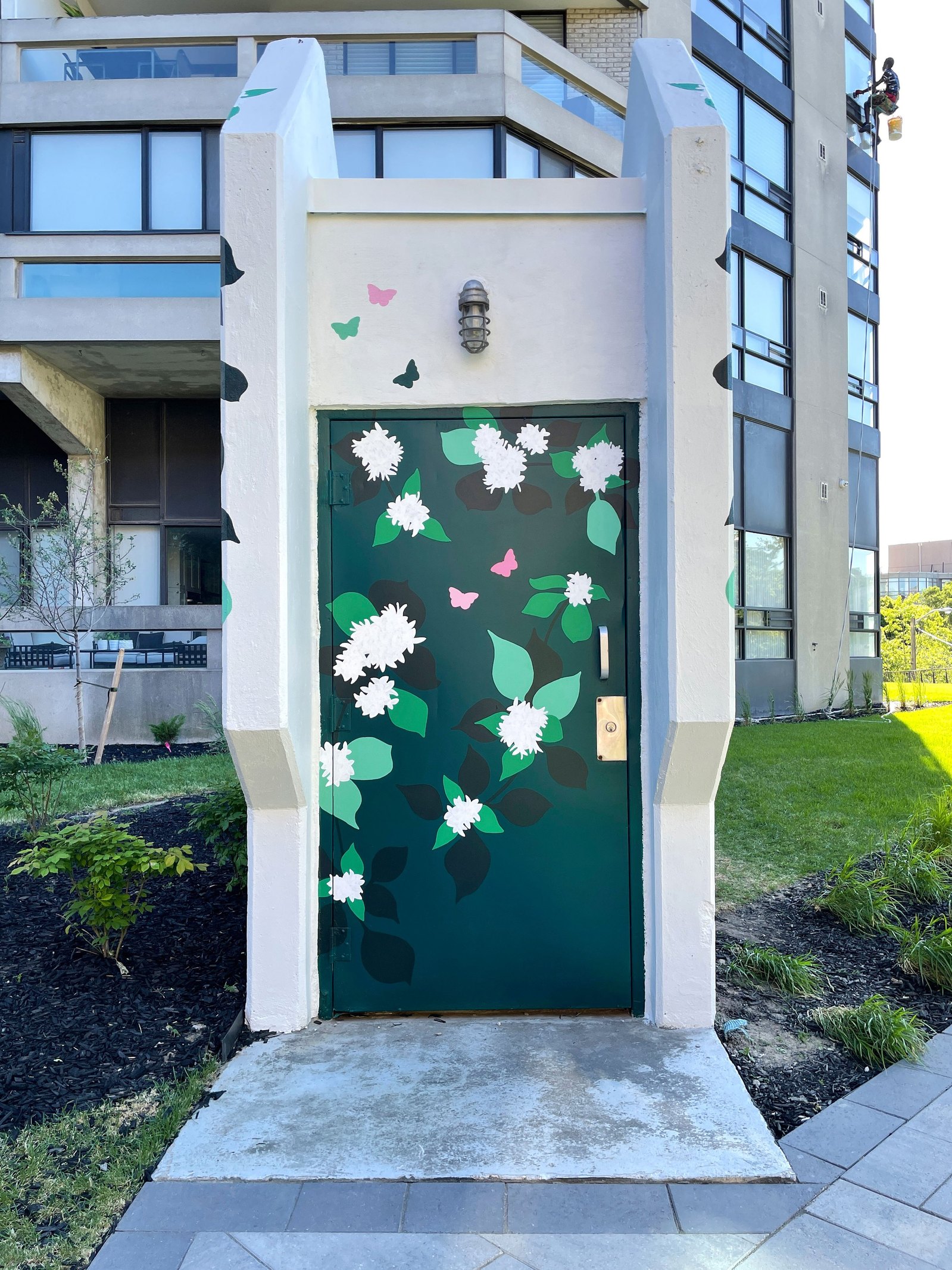 The doorway to a parking garage is painted dark green. White flowers and green leaves add an organic pattern to the structure. 