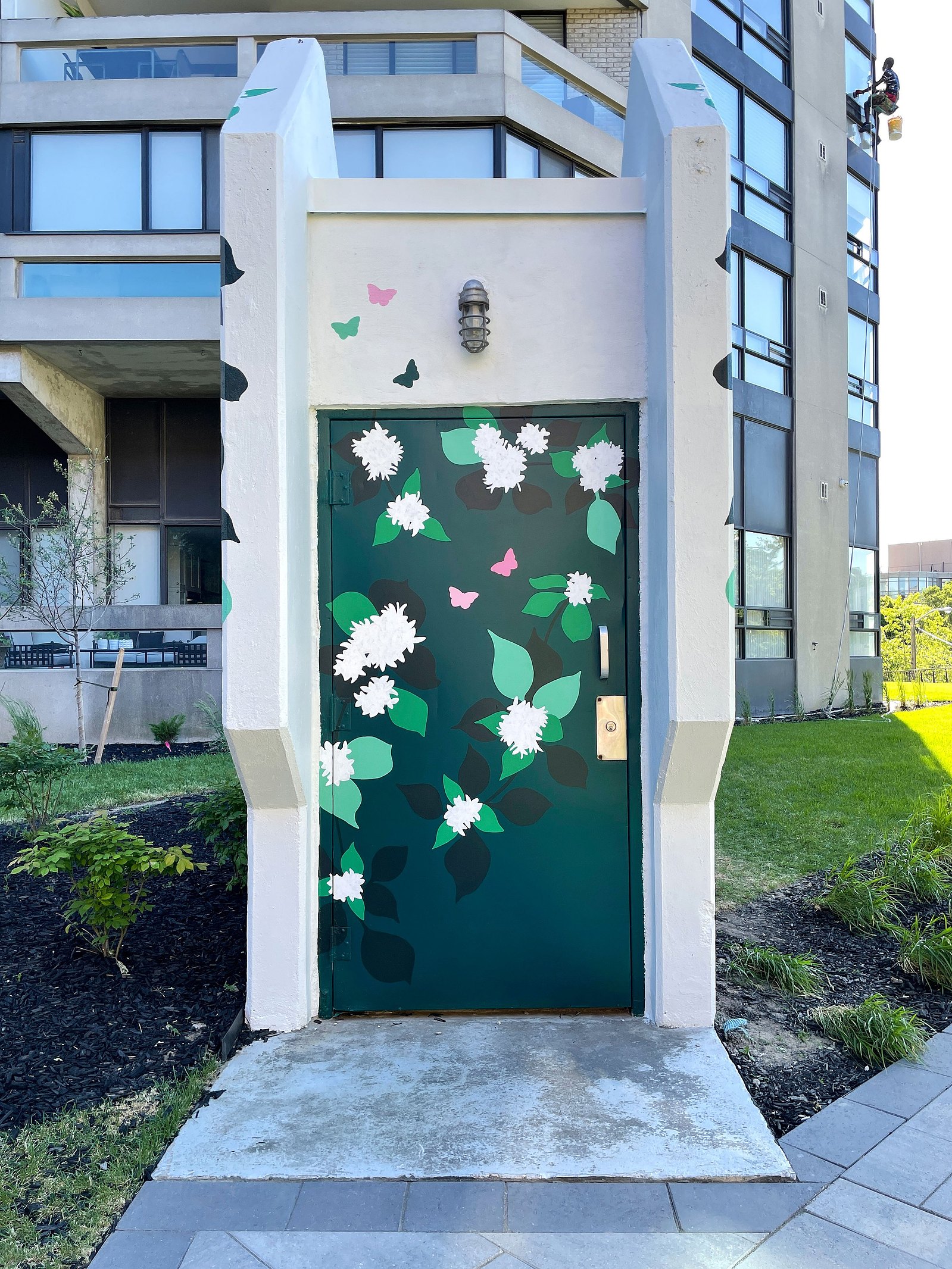 The doorway to a parking garage is painted dark green. White flowers and green leaves add an organic pattern to the structure. 