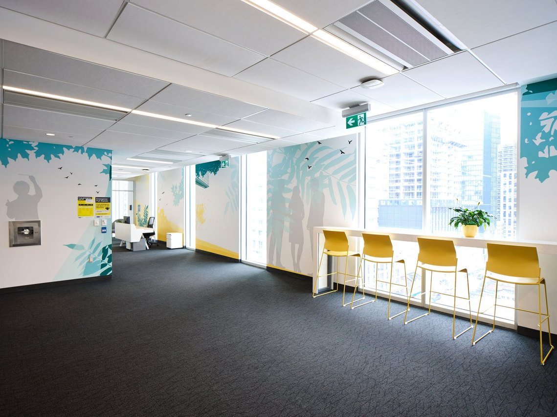 Several murals line a large wall between windows. Yellow rays of light and green foilage add warmth and nature to the office. 