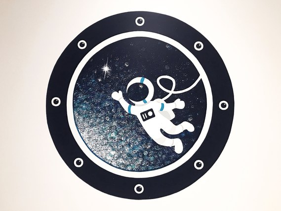 A spaceman waves through a circular spaceship window. 