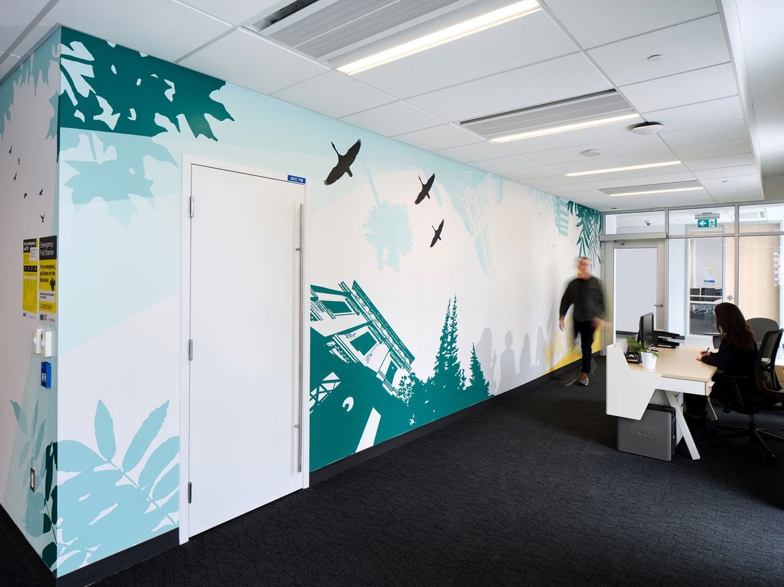 Three Canada Geese guide the way in a biophilic mural of green maple leaves, sumac, and campus buildings. 