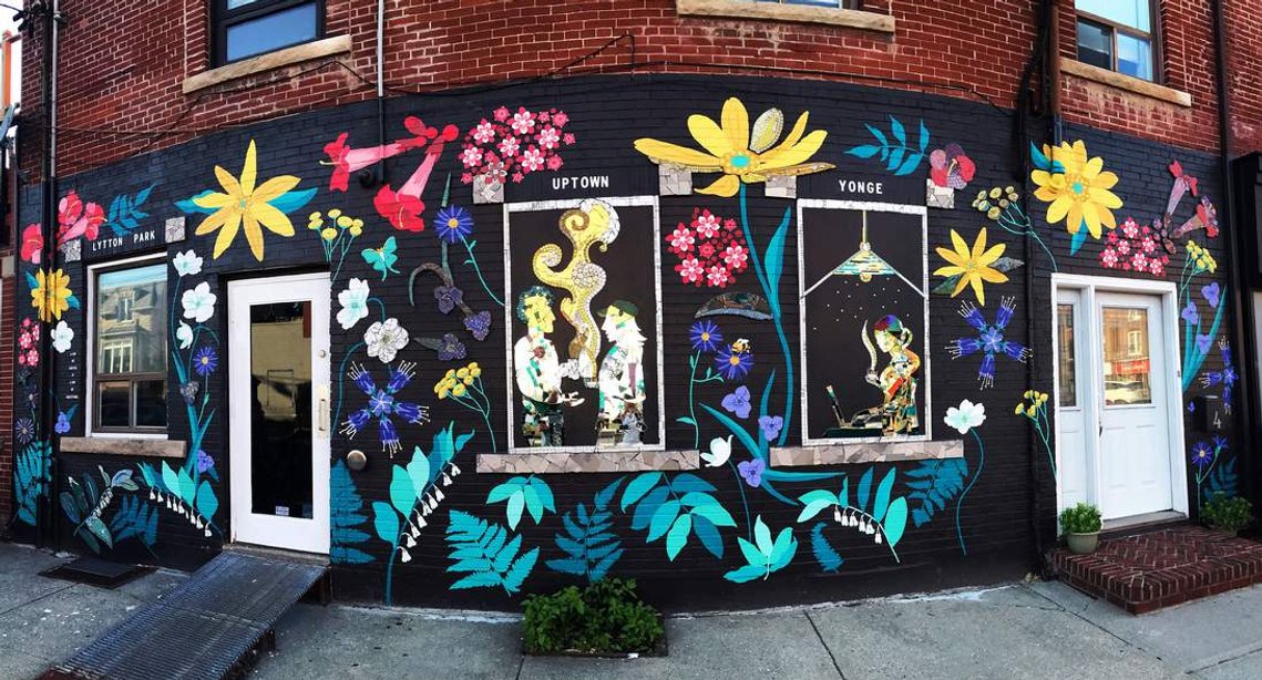 A brick wall painted with a vibrant pattern of  native Ontario flowers on a black background. 
