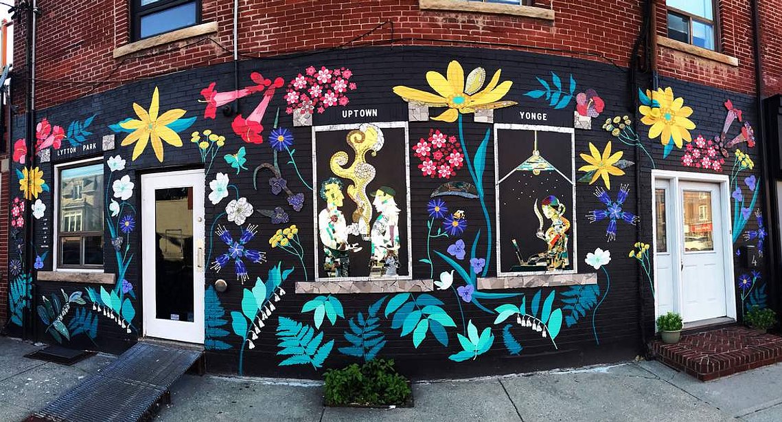 A brick wall painted with a vibrant pattern of  native Ontario flowers on a black background. 