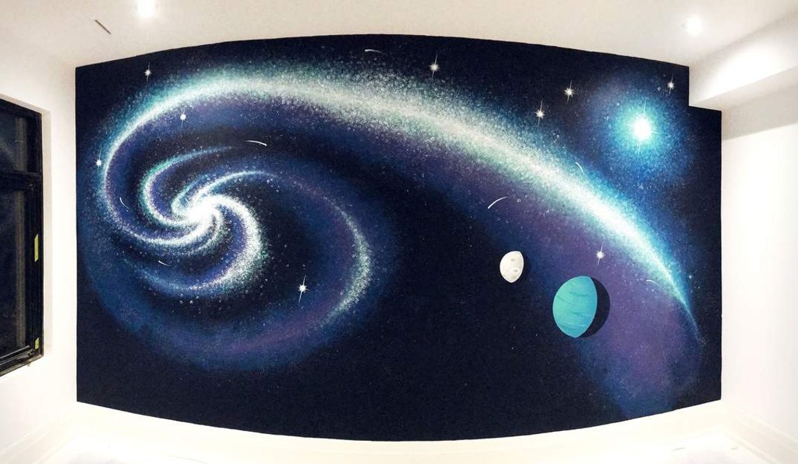 A bedroom mural of outer space with a dark blue night sky and planets, shooting stars, and the Milky Way. 