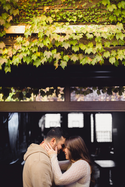 Milwaukee engagement photography session in the Riverwest neighborhood.  Photograph is in color, and the photograph is in Amorphic Beer's beer alley.  Couple are touching foreheads and laughing and smiling.  Changing leaves are at the top of the frame.