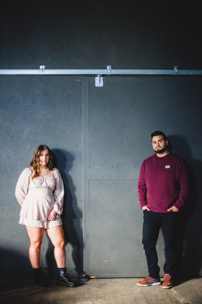 Milwaukee engagement photography session in the Riverwest neighborhood.  At Amorphic Beer, the couple is standing a few feet apart looking at the camera with a serious face.