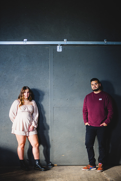 Milwaukee engagement photography session in the Riverwest neighborhood.  At Amorphic Beer, the couple is standing a few feet apart looking at the camera with a serious face.