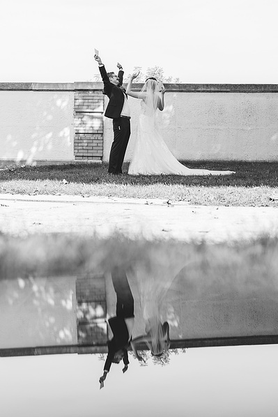 black and white photograph of bride and groom on their wedding day in milwaukee, wisconsin.  bride and groom have both arms in the air in celebration and the shot is reflected on a shiny surface.