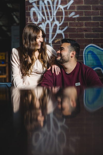 Milwaukee engagement photography session in the Riverwest neighborhood.  Inside of Amorphic Beer in front of graffiti wall and reflections of a table.