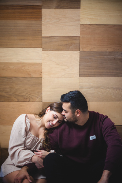 Milwaukee engagement photography session in the Riverwest neighborhood.  at Amorphic Beer, the couple is sitting in front of a wood paneled wall, not looking at the camera but snuggling their heads close together.