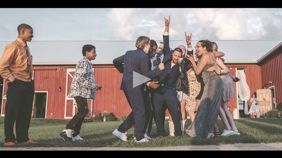 still from a wedding day video showing the groom being mobbed by guests of the wedding in celebration.  He is holding up his hands in celebration, and everyone is smiling and laughing.