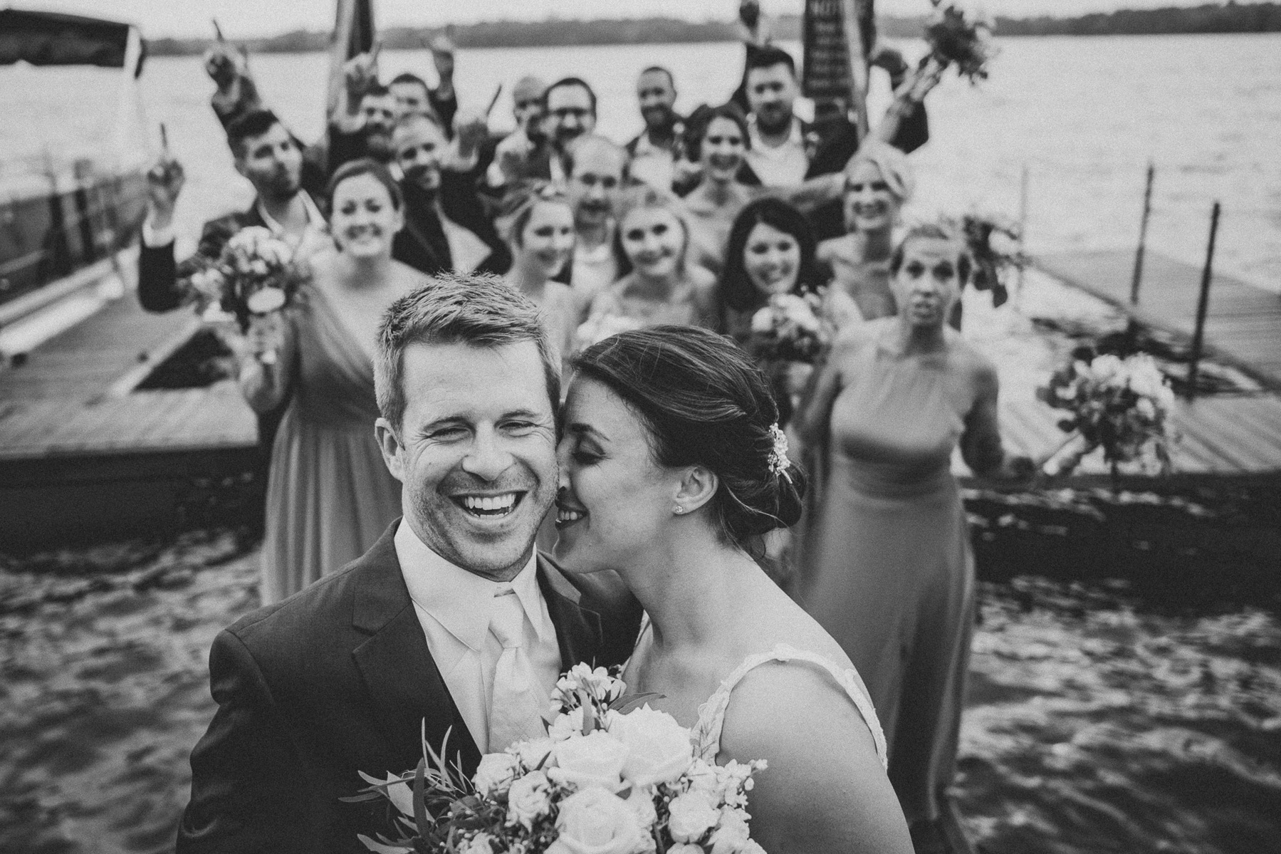 Bridal party wedding photo in black-and-white, bride and smiling and kissing the girl while groom looks at camera