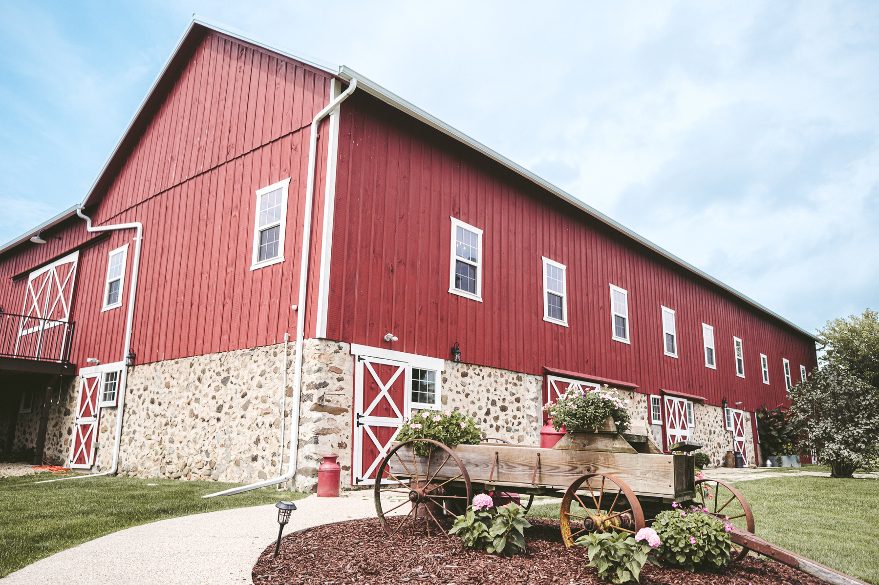 Folk Song Farm as one of the top wedding venues in Milwaukee.  Barn wedding venue, this photo shows a wide perspective of the outside of the barn, which is painted red with bricks on the lowest level and a blue sky.  Wagon in the foreground.