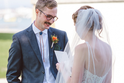 bride reads vows to the groom during the first look on their wedding day.  First look is taking place at south shore terrace in milwaukee, wisconsin.  Shot is over the brides shoulder, focusing on the grooms face, which is smiling.