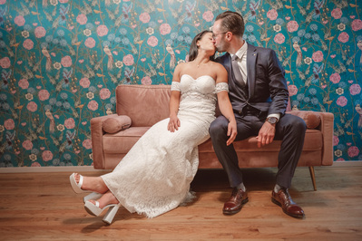 Milwaukee Wedding Photography, Chicago Wedding Photography.  Couple kisses while sitting on couch in front of floral wallpaper.