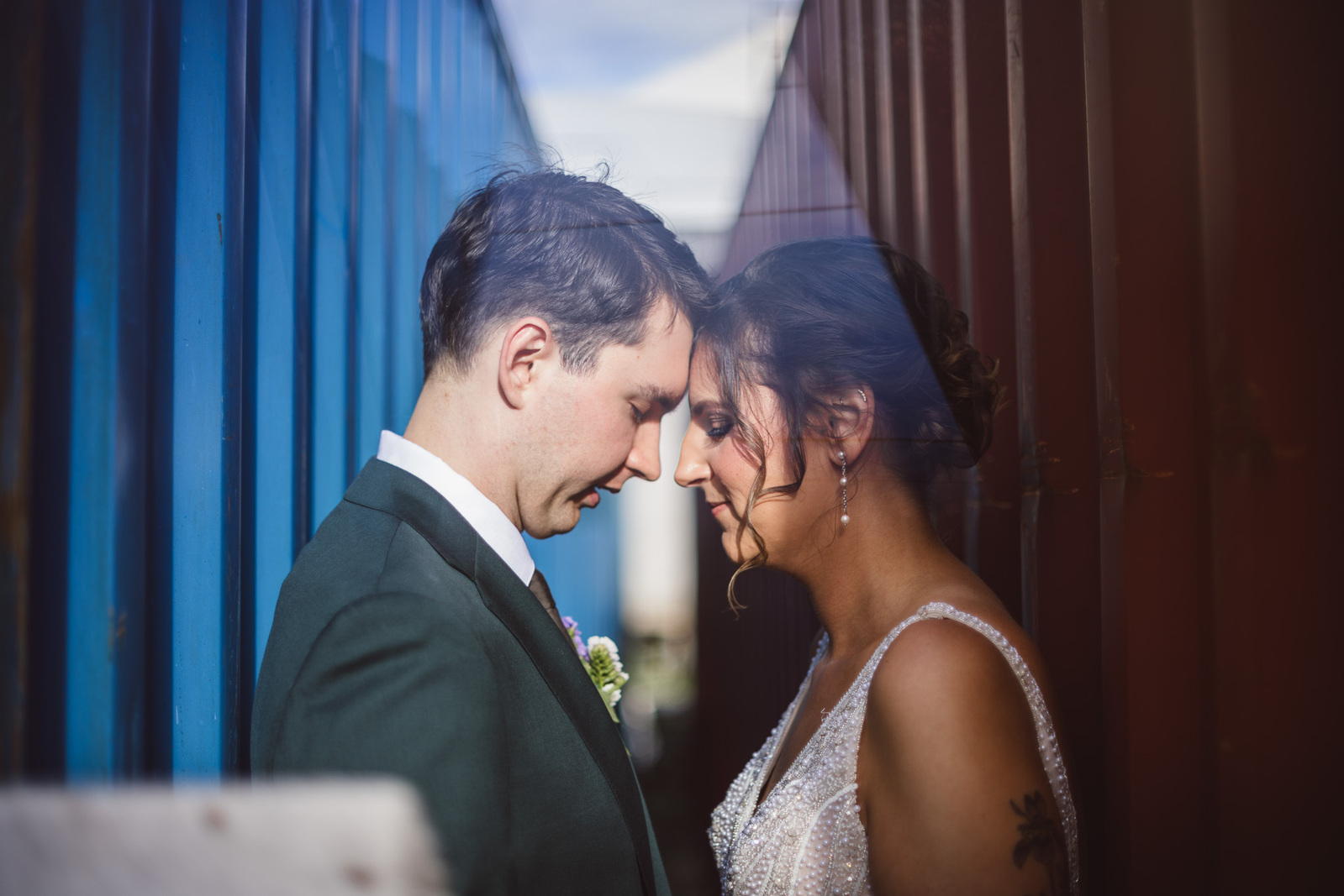 milwaukee wedding couple stands touching foreheads.  wedding day, bridal portraits, symmetrical.  shipping containers in blue and red, couple stands in good light.