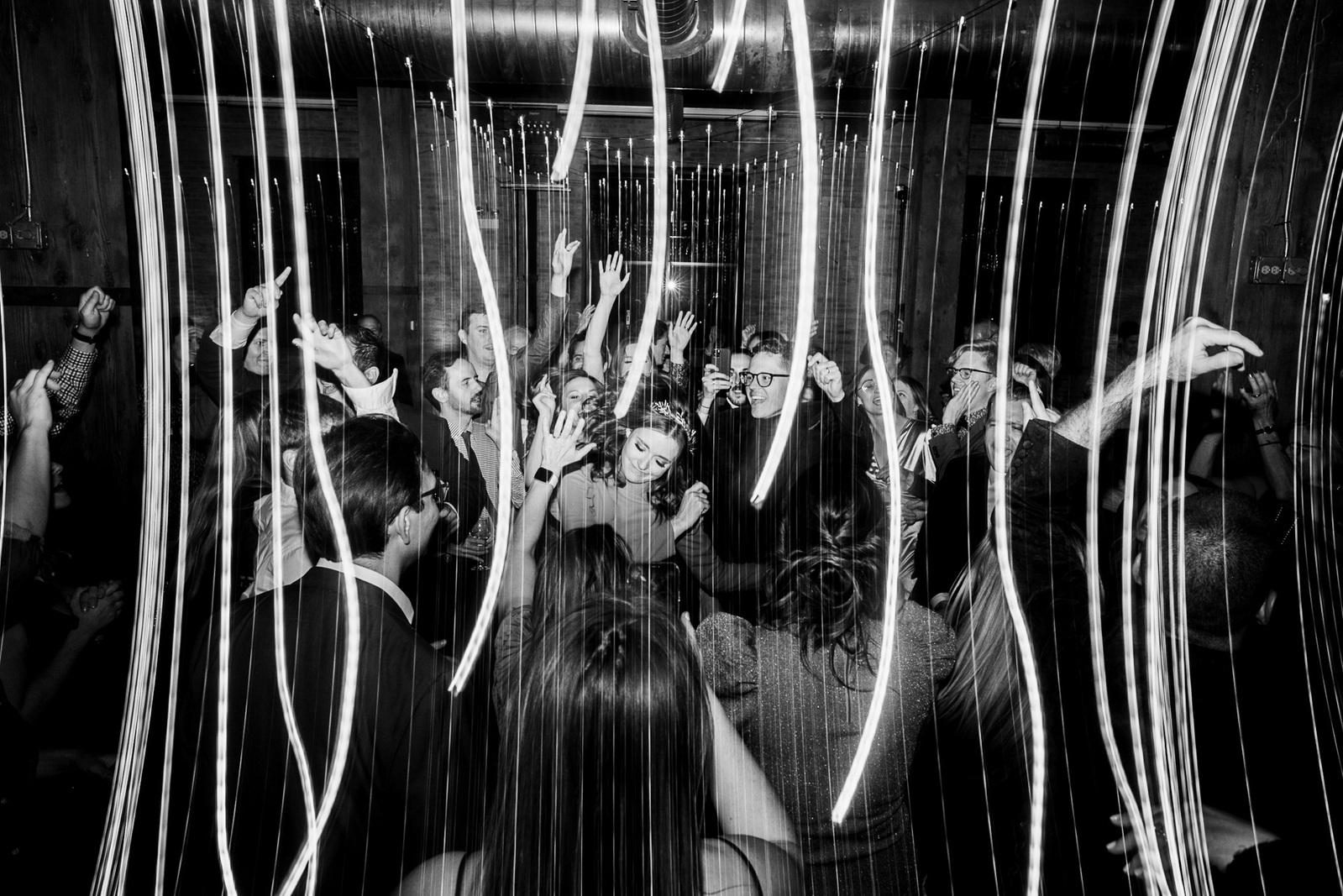 Milwaukee wedding photography black and white wedding dancefloor shot.  streaming lights, dragged shutter, couple dancing in the middle of large crowd.  bride is smiling.  Chicago wedding at the Lacuna Lofts.