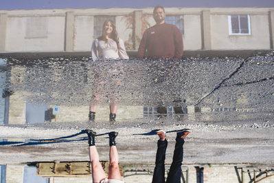 Milwaukee engagement photography session in the Riverwest neighborhood.  Standing in front of Amorphic Beer, couple is reflected in a puddle in the parking lot.  Engagement shoot wardrobe is blouse and shorts and pants and sweater.