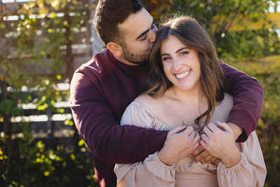 Milwaukee engagement photography session in the Riverwest neighborhood.  Couple smiling while looking at the camera. couple stands in front of a fence.