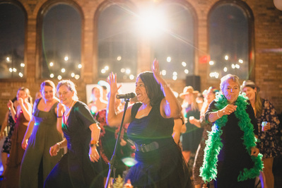 south shore terrace in milwaukee wisconsin, the live band plays and sings with wedding guests dancing behind them during a wedding reception.