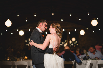 bride and groom dance during the wedding reception at south shore terrace in Milwaukee wisconsin.  color photograph with lights from the ballroom behind them, the bride and groom are smiling at one another.