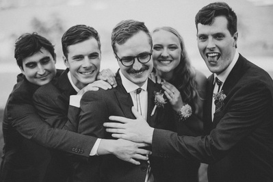 groom and groomsmen plus sister are embracing in a black and white photograph on the wedding day in milwaukee wisconsin at south shore terrace.  groom is looking down and smiling, while his groomsmen and sister are putting their hands on his shoulders.
