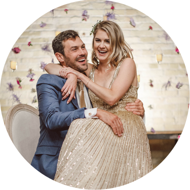 couple sitting and laughing on their wedding day.  Bride is in Groom's lap, with hanging decorations in the background.  This is a Milwaukee wedding at the Pritzlaff Building and Events, photograph taken by Patrick Betcher of Betcher Photo.