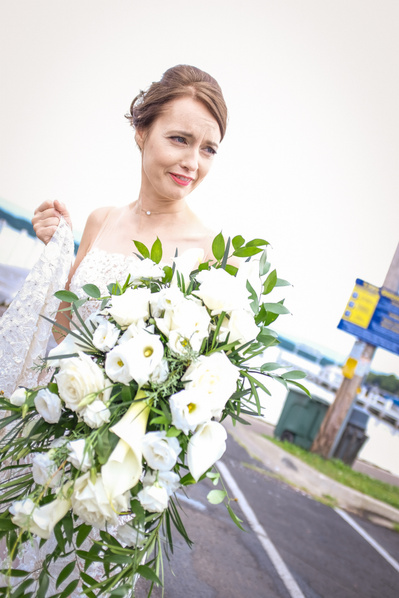 candid photograph of bride holding a large bouquet of white flowers with a grin on her face.