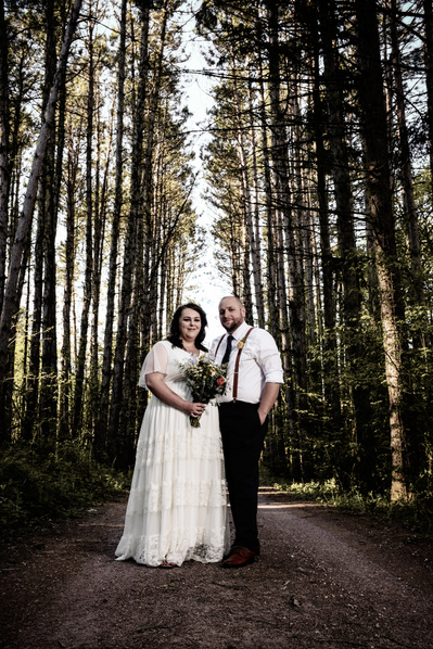 Bride and groom standing side by side in classic bridal portrait on a dirt road with a long line of tall trees surrounding them.