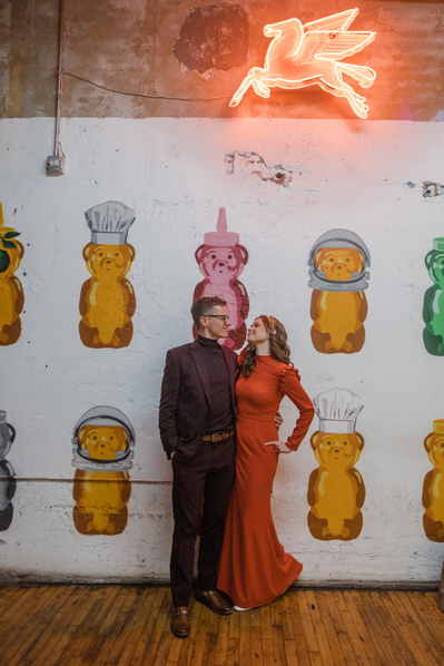 bride and groom standing side by side in front of colorful wall and neon pegasus sign.