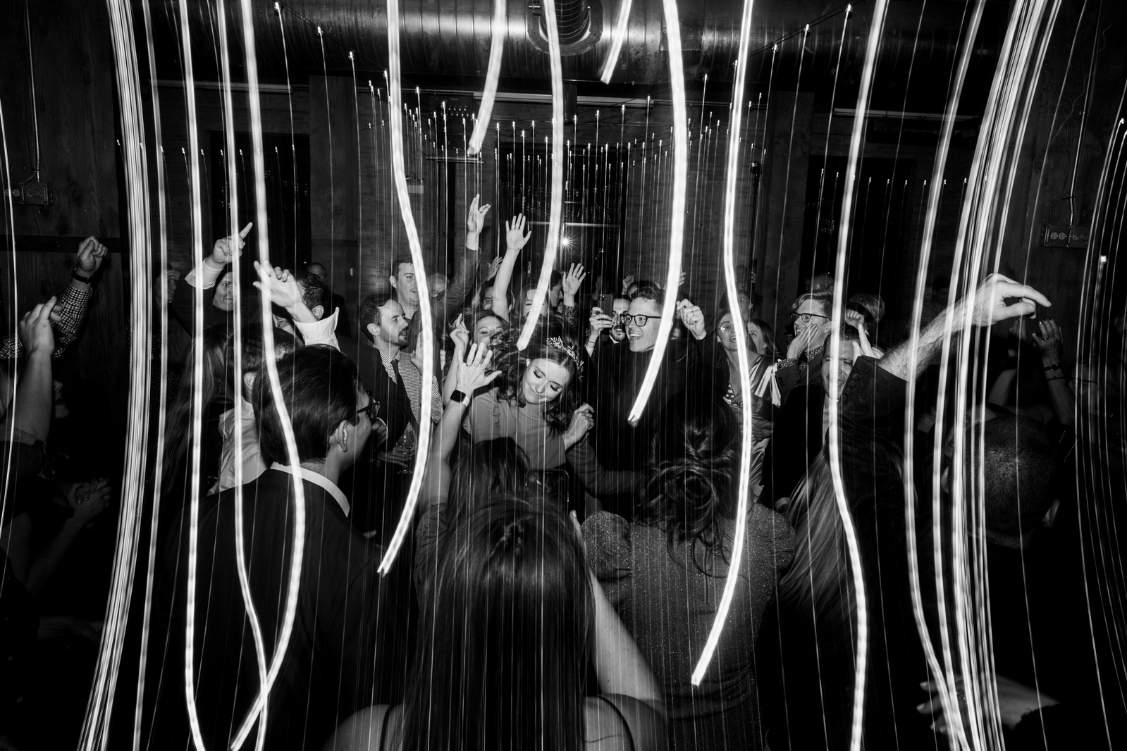 wedding couple dances in black and white with light streaks.  guests surround them and everyone is dancing and having a great time.