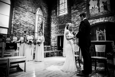 black and white photograph of bride and groom at the altar with bridesmaids in the background.