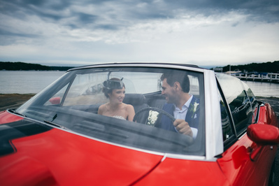 bride and groom sitting in red classic car in front of a lake in Lake Geneva, Wisconsin.