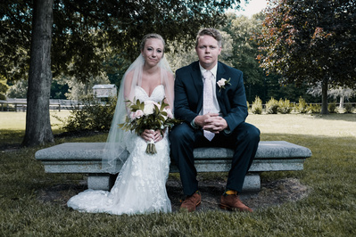 bride and groom portrait sitting on a bench side by side with serious look on face.