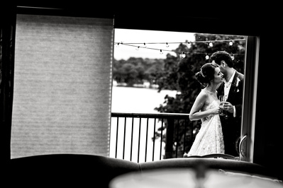 bride and groom embracing on balcony, picture is taken from inside and through a window.
