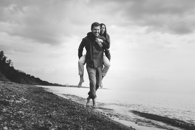 Couple giving piggyback ride along the beach in black-and-white photo. Smiling on Lake Michigan in Wisconsin