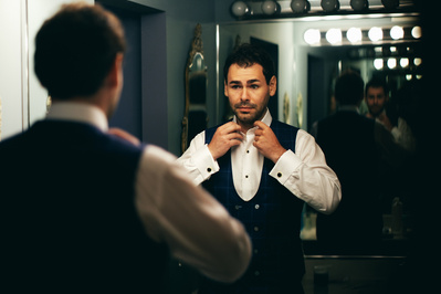groom preparing by fixing his shirt and tie in the mirror.