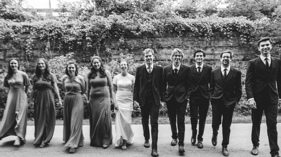 Bridal party photograph on their wedding day with bridesmaids on the left and groomsmen on the right.  Bride and Groom are in the middle, and the group is walking towards the camera, smiling.