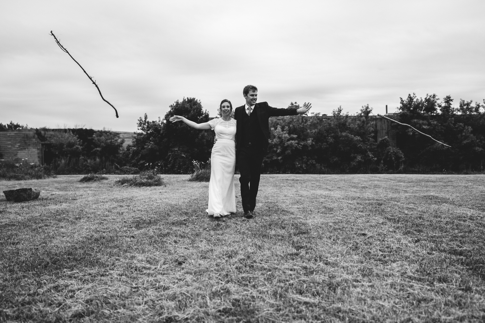 black and white photo of couple, bride and groom standing in a field tossing sticks.  Married at the Urban Ecology Center in Milwaukee, Wisconsin.  Summer wedding, laid back and low key.