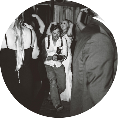 Photographer Patrick Betcher of Betcher Photo taking photographs on the dancefloor at a wedding in the Milwaukee area.  Holding a camera and smiling, Patrick is having a great time as a professional wedding photographer.