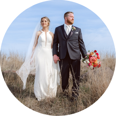 bride and groom hold hand in a field of tall grass on their wedding day in Milwaukee, Wisconsin.  Groom is holding a bouquet of flowers while the bride holds on to her dress.  The both look off into the distance.
